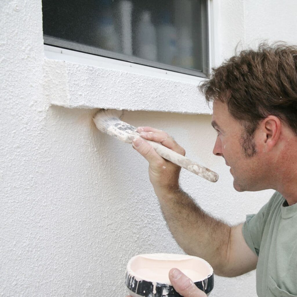 man repainting the side of a home