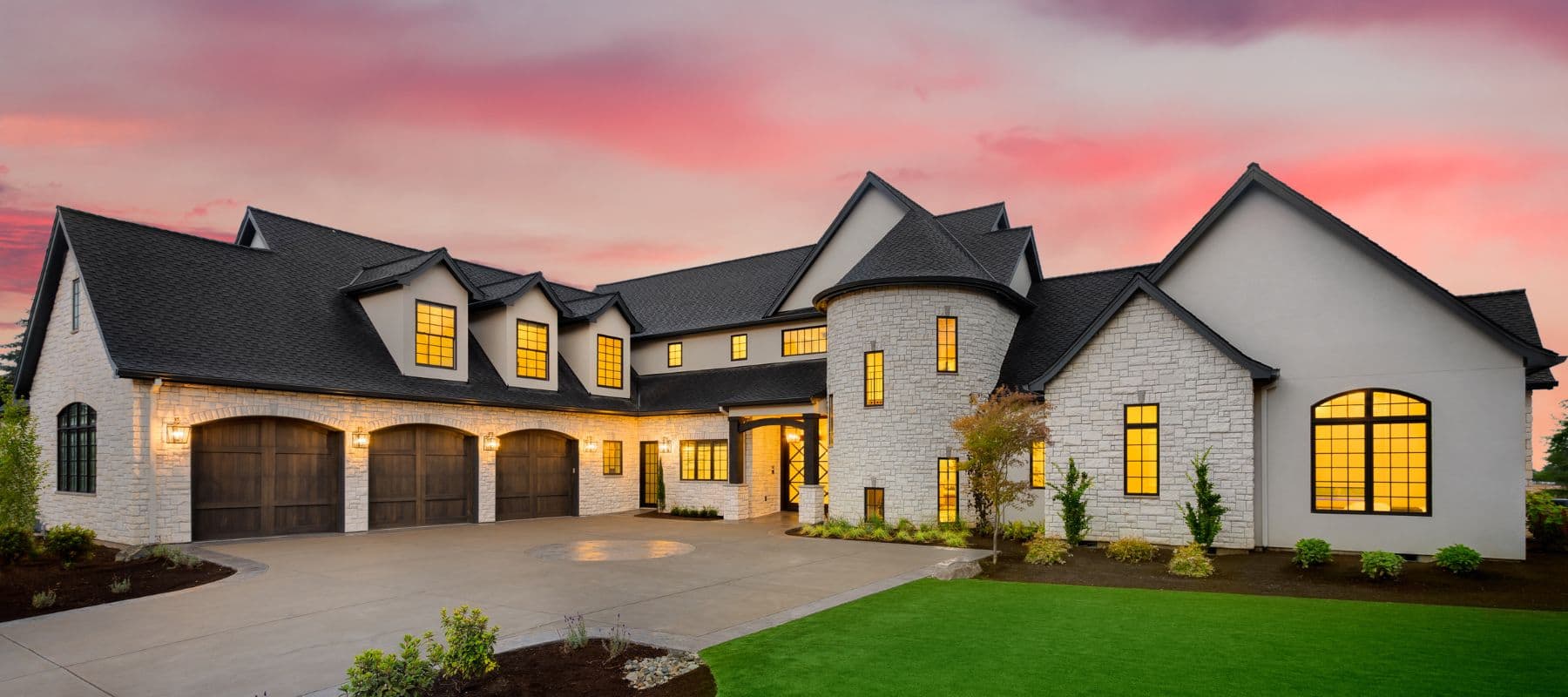 Large luxury home with dark roof shingles and stone exterior at sunset