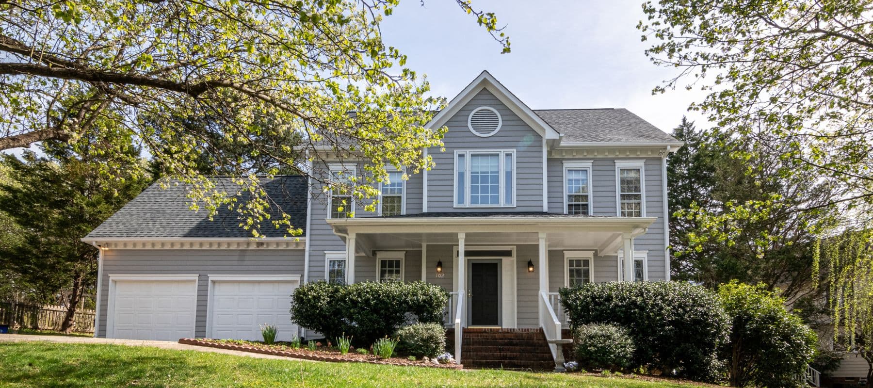 Gray suburban house with front porch, double garage, and lush landscaping